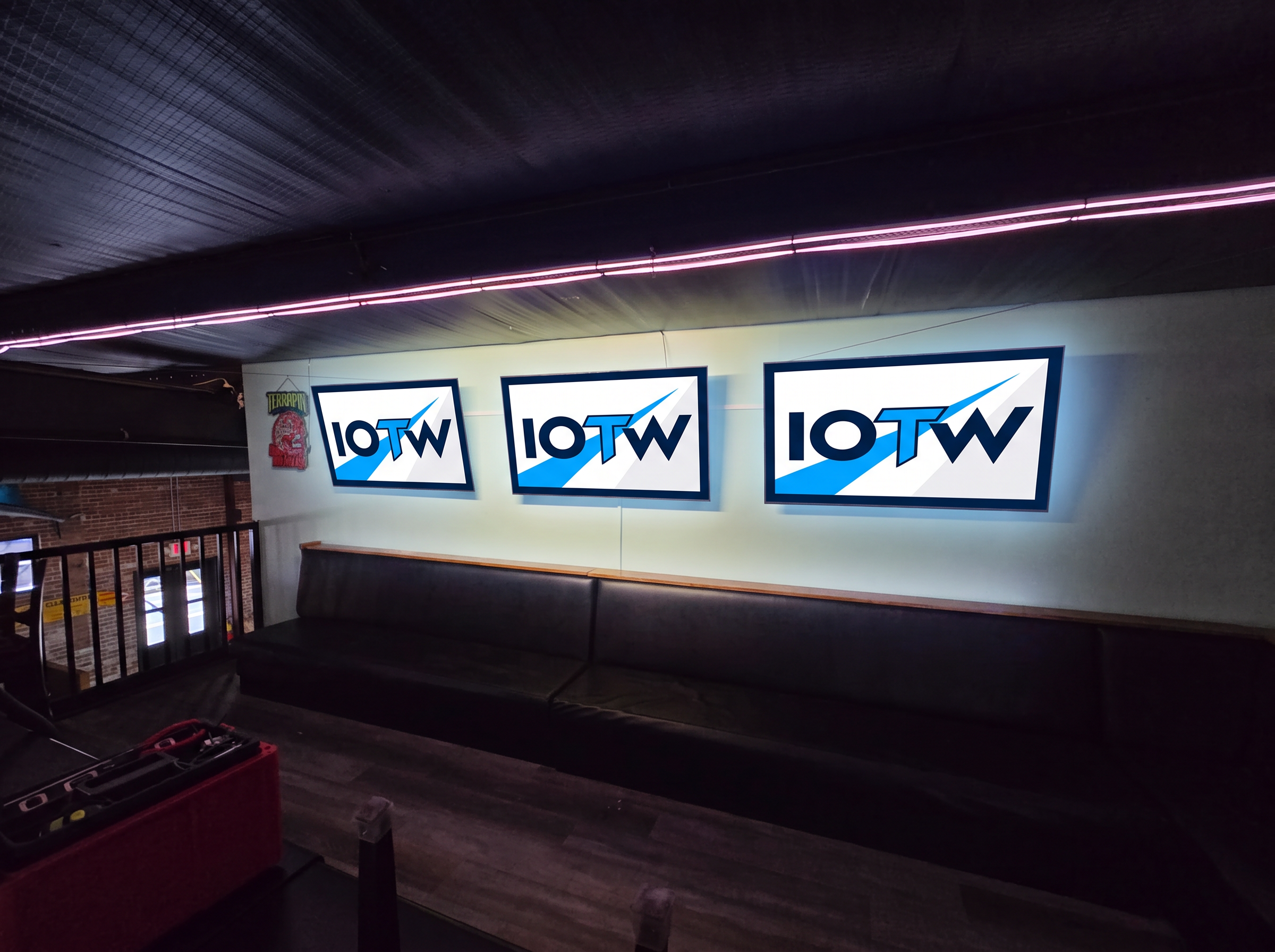 Three TVs mounted in a row above booth seating in a sports bar